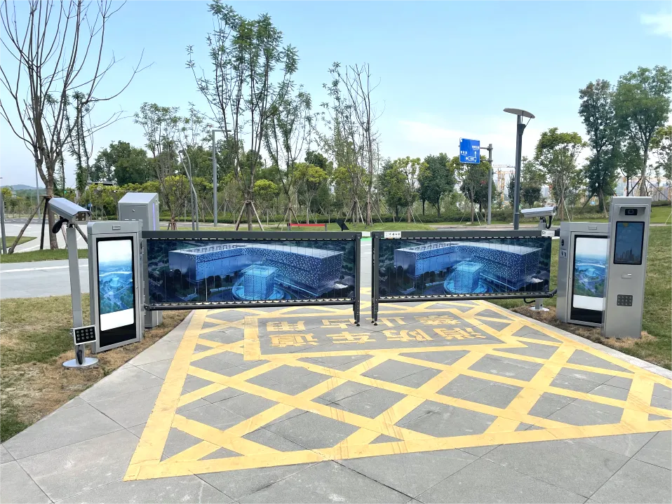 Automated gate entrance with barriers displaying aquarium images, yellow caution markings on the ground, ticket machines on both sides, and trees and grass in the background.
